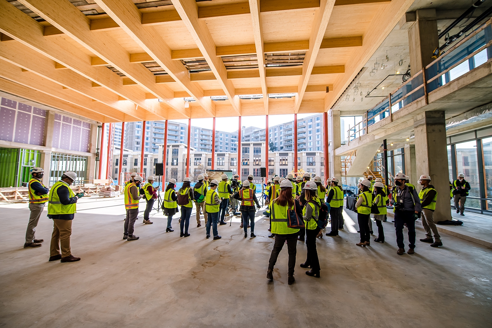 An image of people touring the construction site of Amazon's second headquarters while wearing hard hats that say "Amazon" and bright yellow safety vests.