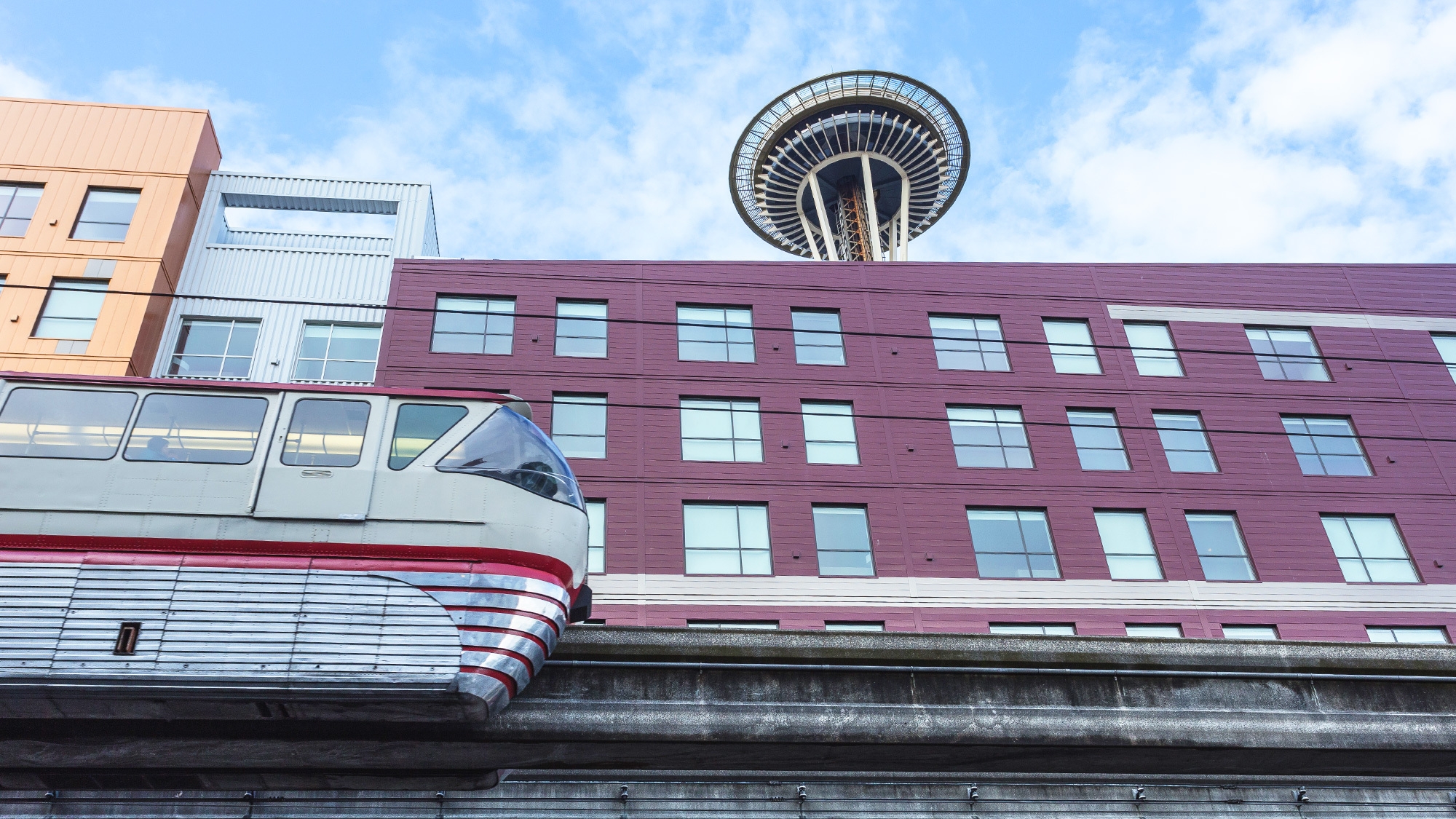 A train passes by a housing complex with the Seattle Space Needle in the skyline.