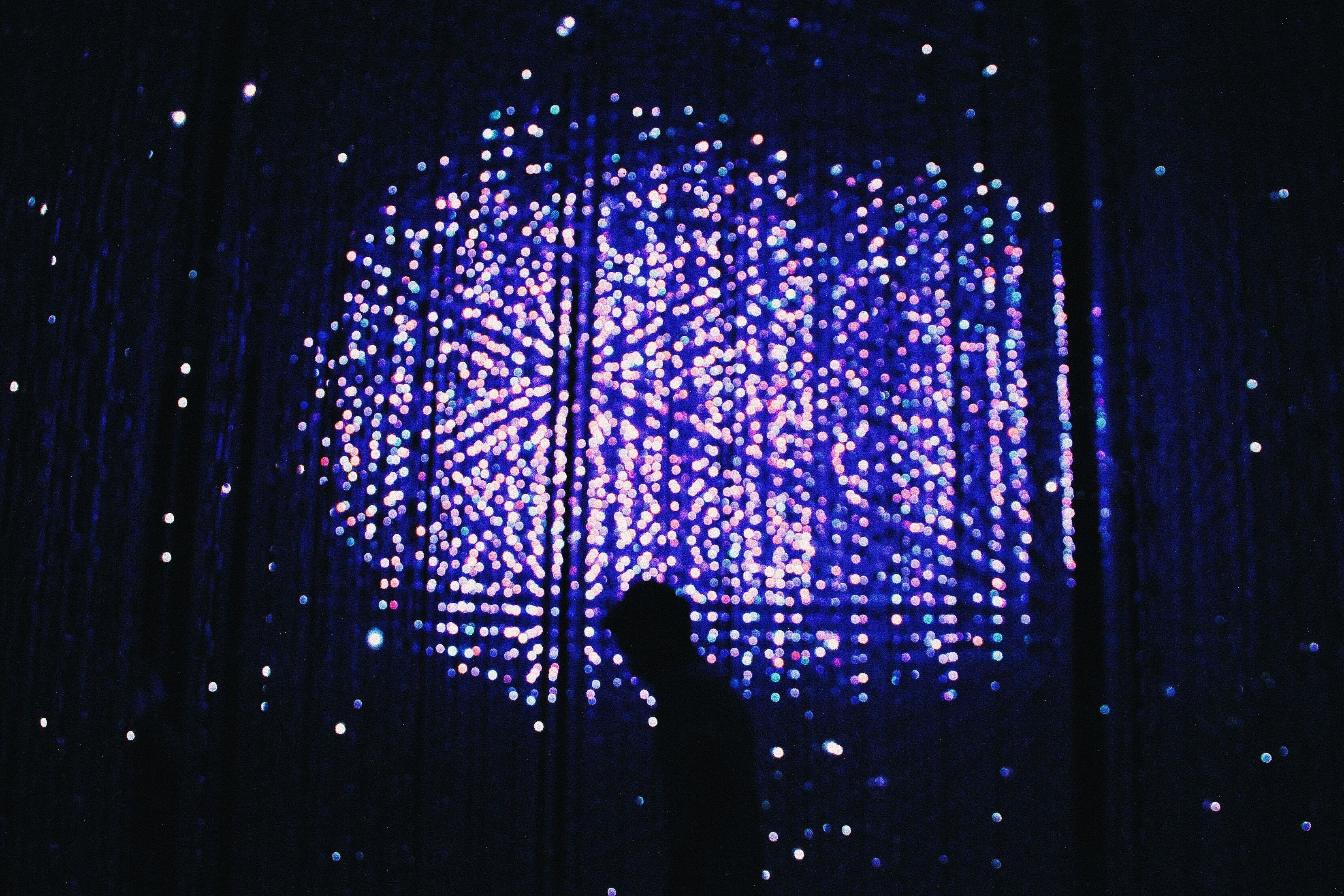 Image of a man walking in front of a wall of lights at night