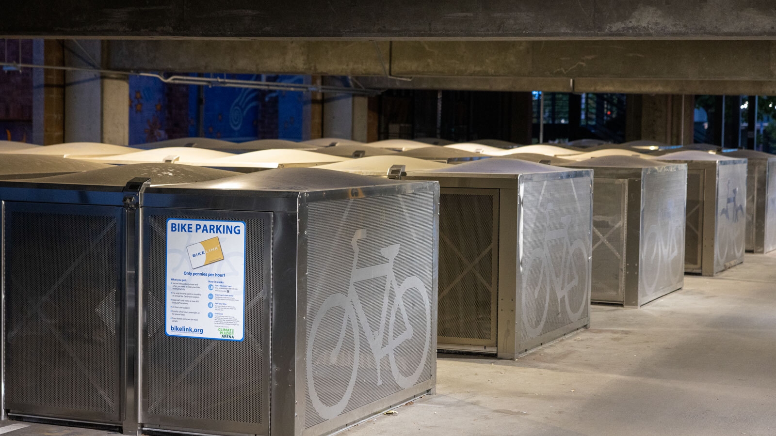 an image of several large, metal boxes with bicycle symbols painted on them. there is a sign showing that they are for bike parking.