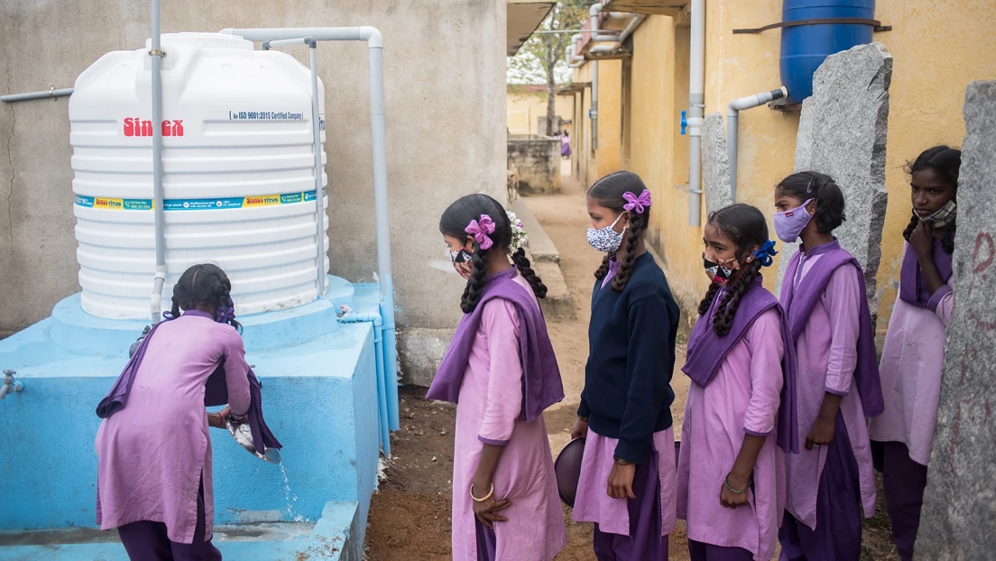 An image of six girls lining up to get water waring purple uniforms. 