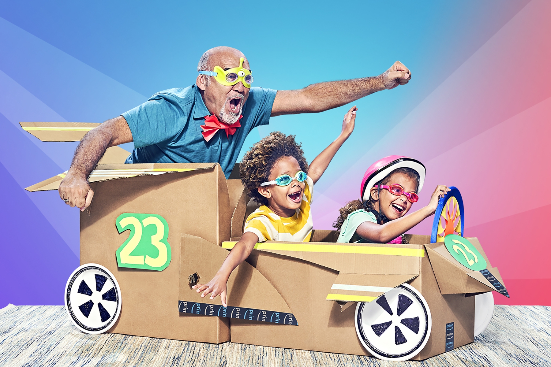 Two children and a man appear joyful as the "ride" in a cardboard box car. 