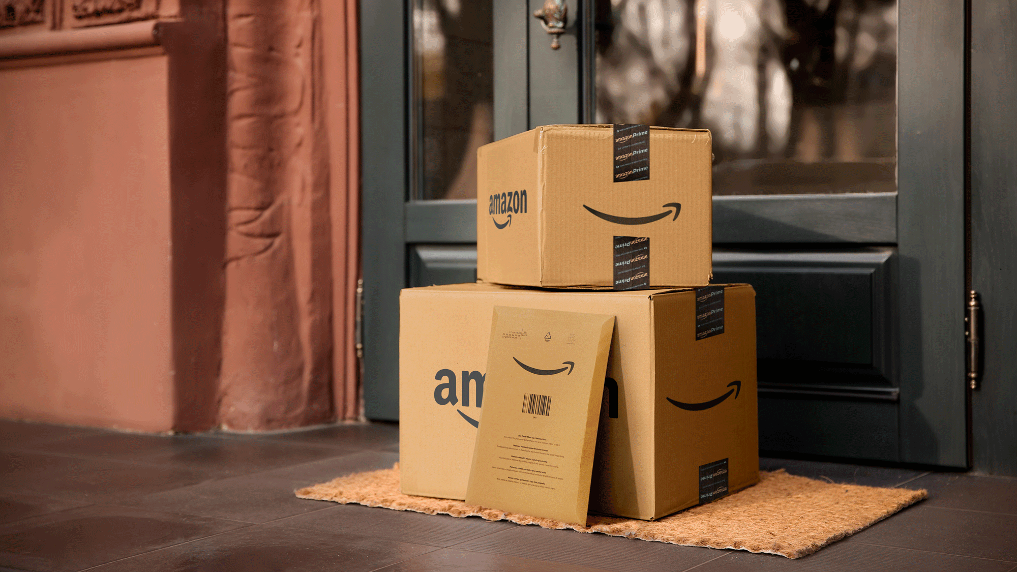 An image of two Amazon delivery boxes and an envelope on the floor next to a front door.  