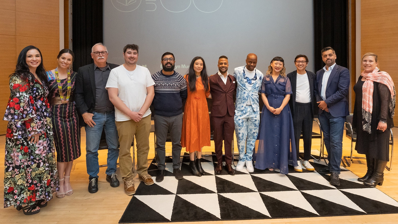 A photo of 12 people on the stage of the the National Book Foundation' 5 Under 35 Reception 2023 at the Brooklyn Museum.