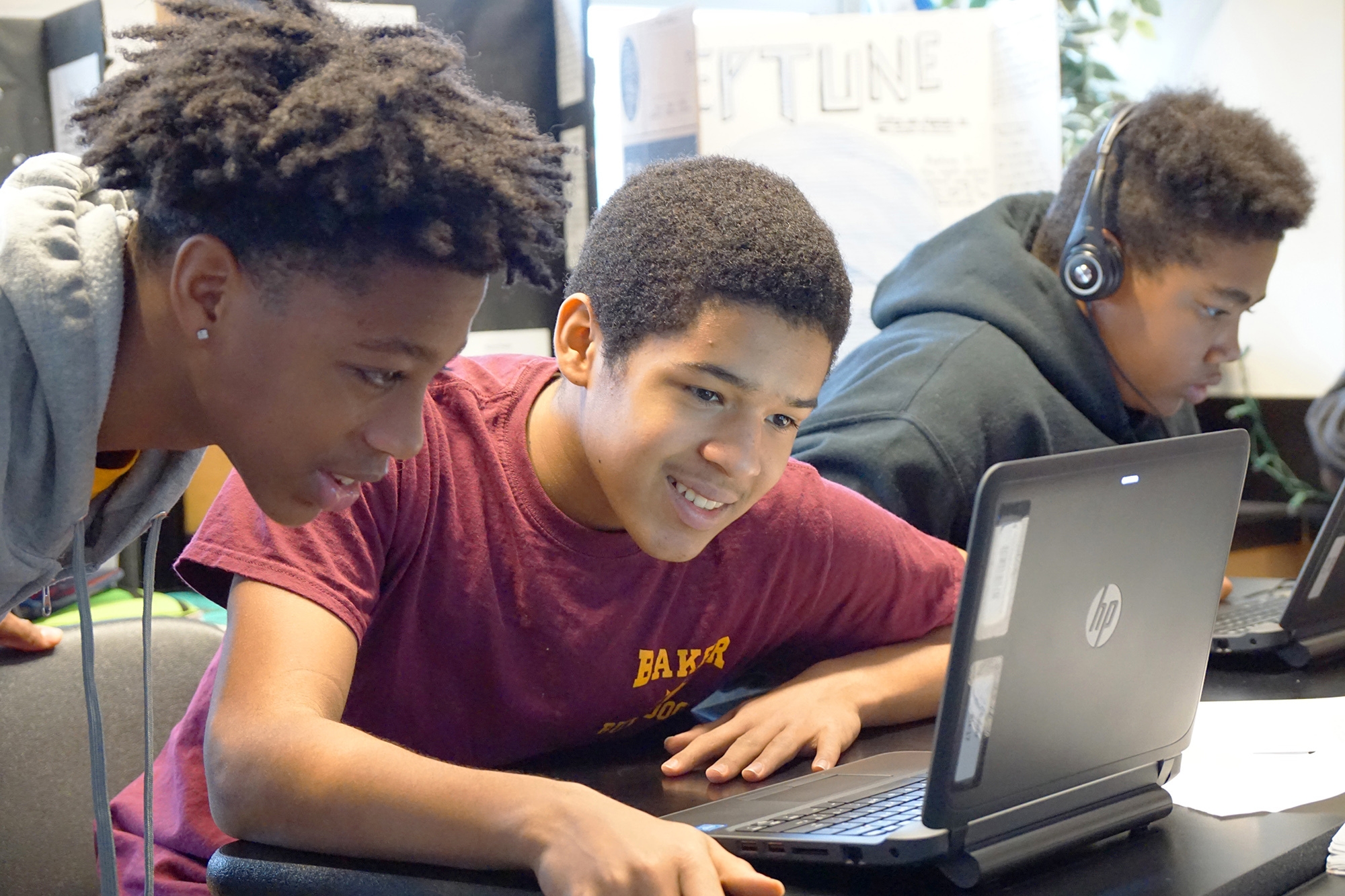 Students use a laptop in a classroom while working together on a coding project.