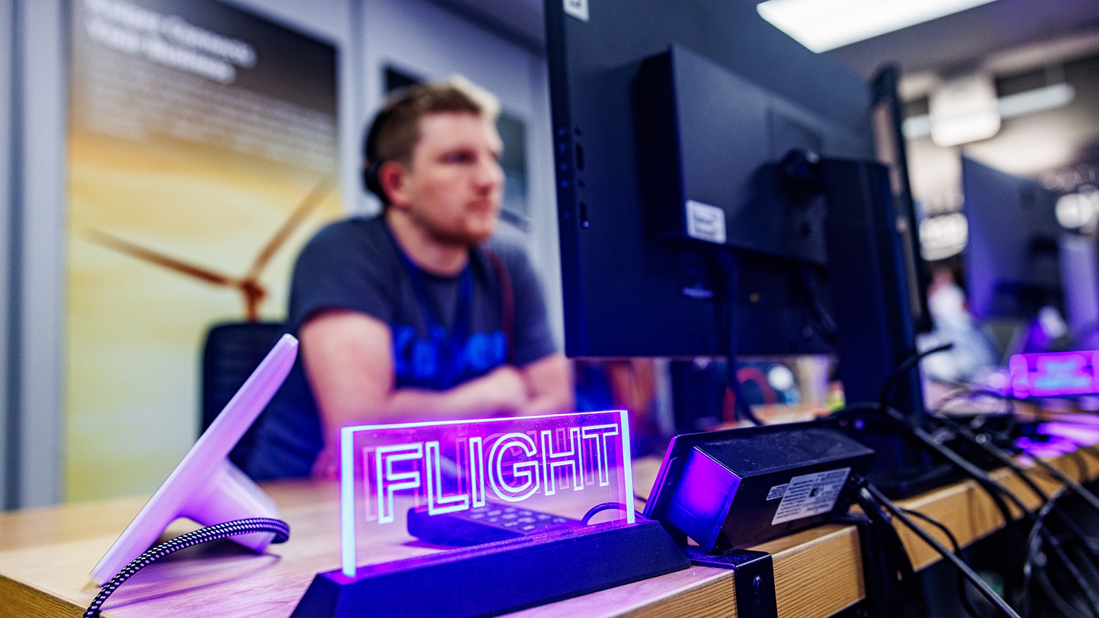 An image of a person from Project Kuiper’s mission management team working on a computer. There is a neon sign sitting on the desk that reads "FLIGHT"