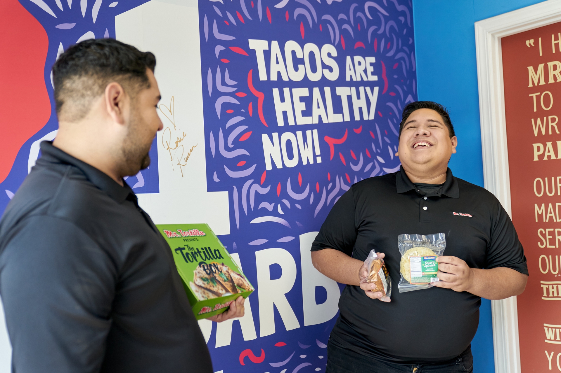 Ronald and Anthony  hold their products in front of a Mr. Tortilla promotional sign.