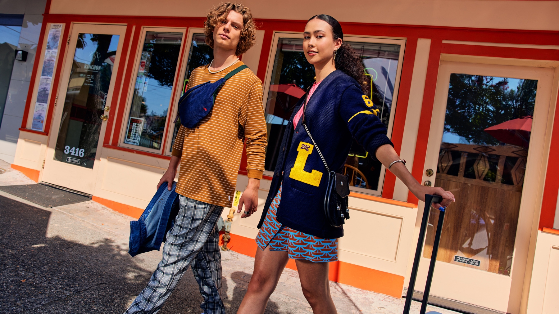 An image of two college students walking out of a store and looking at the camera. They are wearing colorful outfits.  