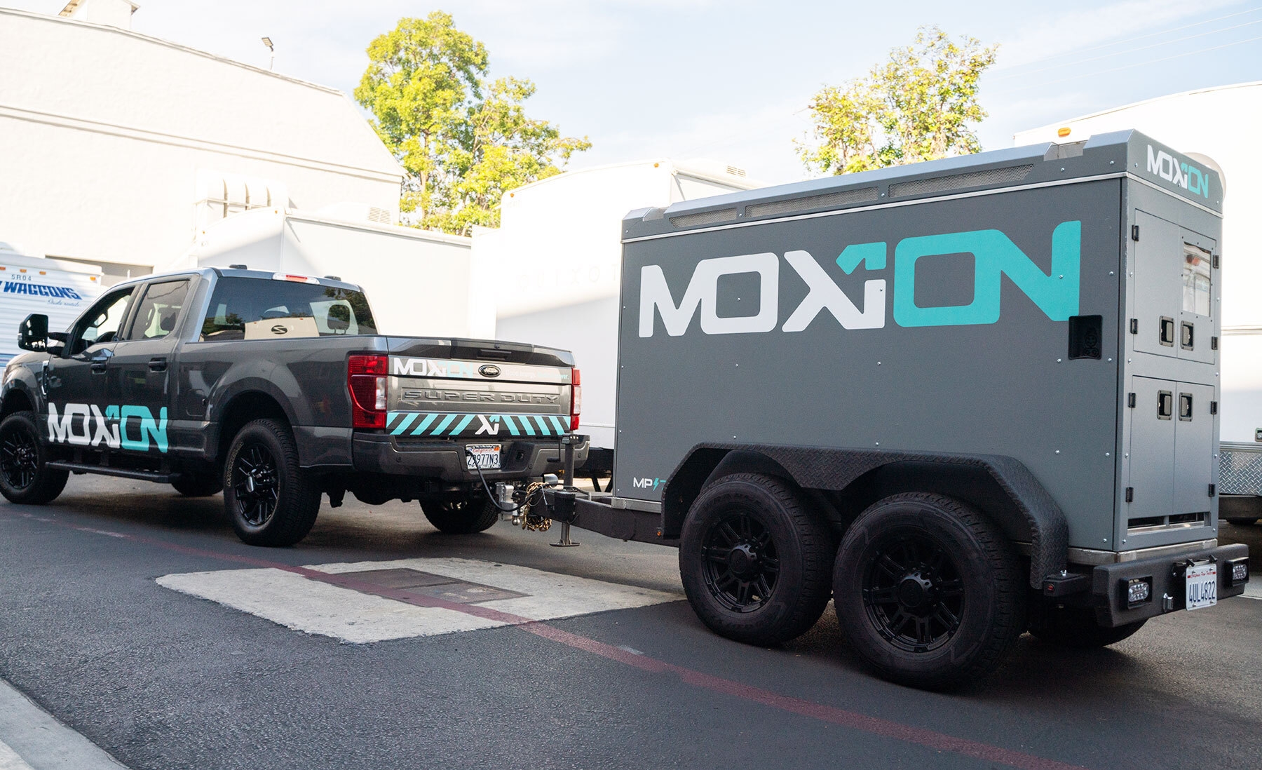 A truck towing a small trailer in the backlots of a movie studio, both with the Moxion Power logo.