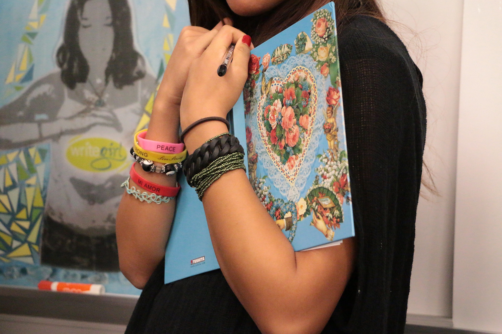 An image of arms holding an open book. The person is wearing a variety of bracelets showing their personality. 