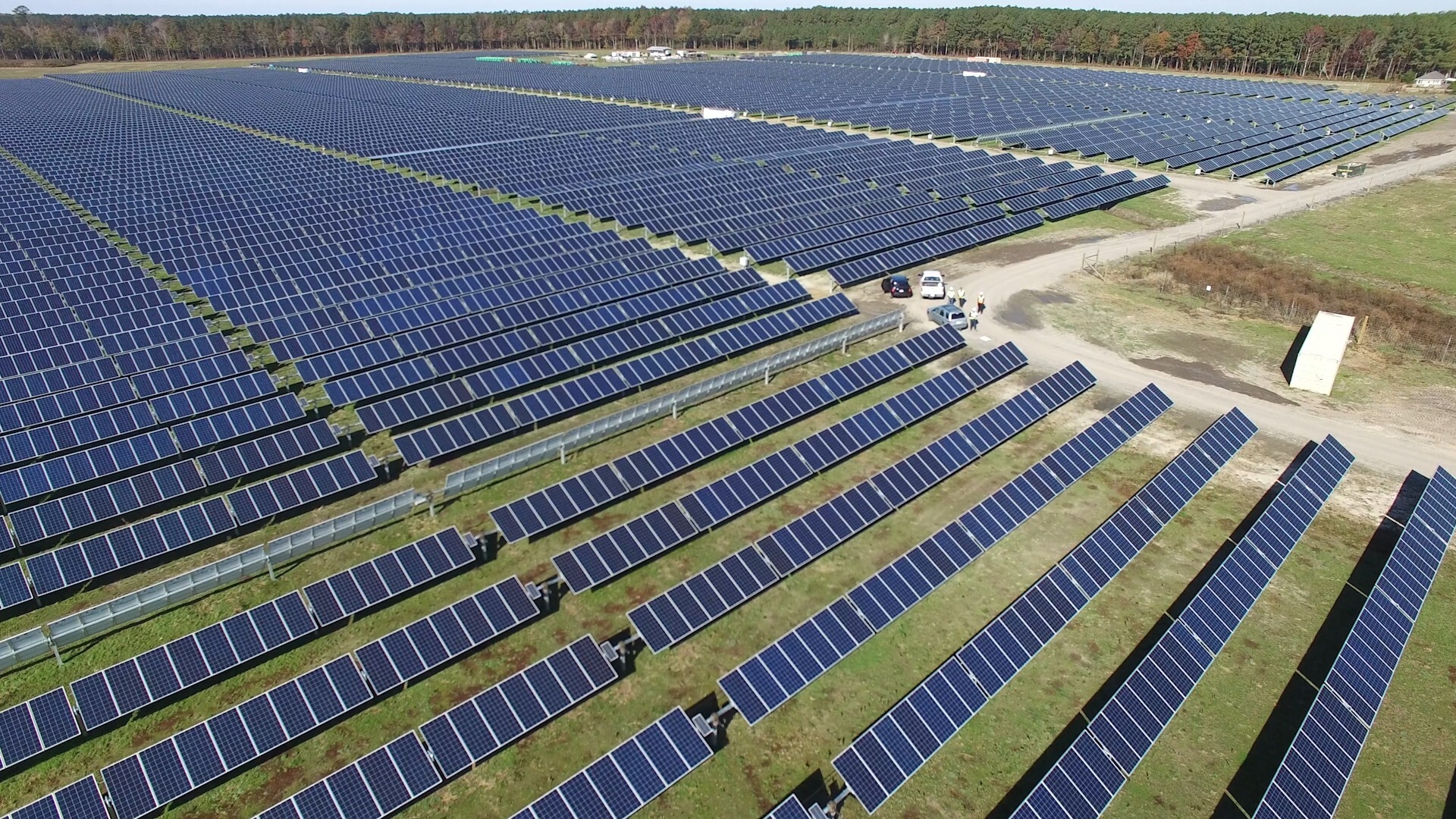 A solar farm with a few cars parked and people looking around.