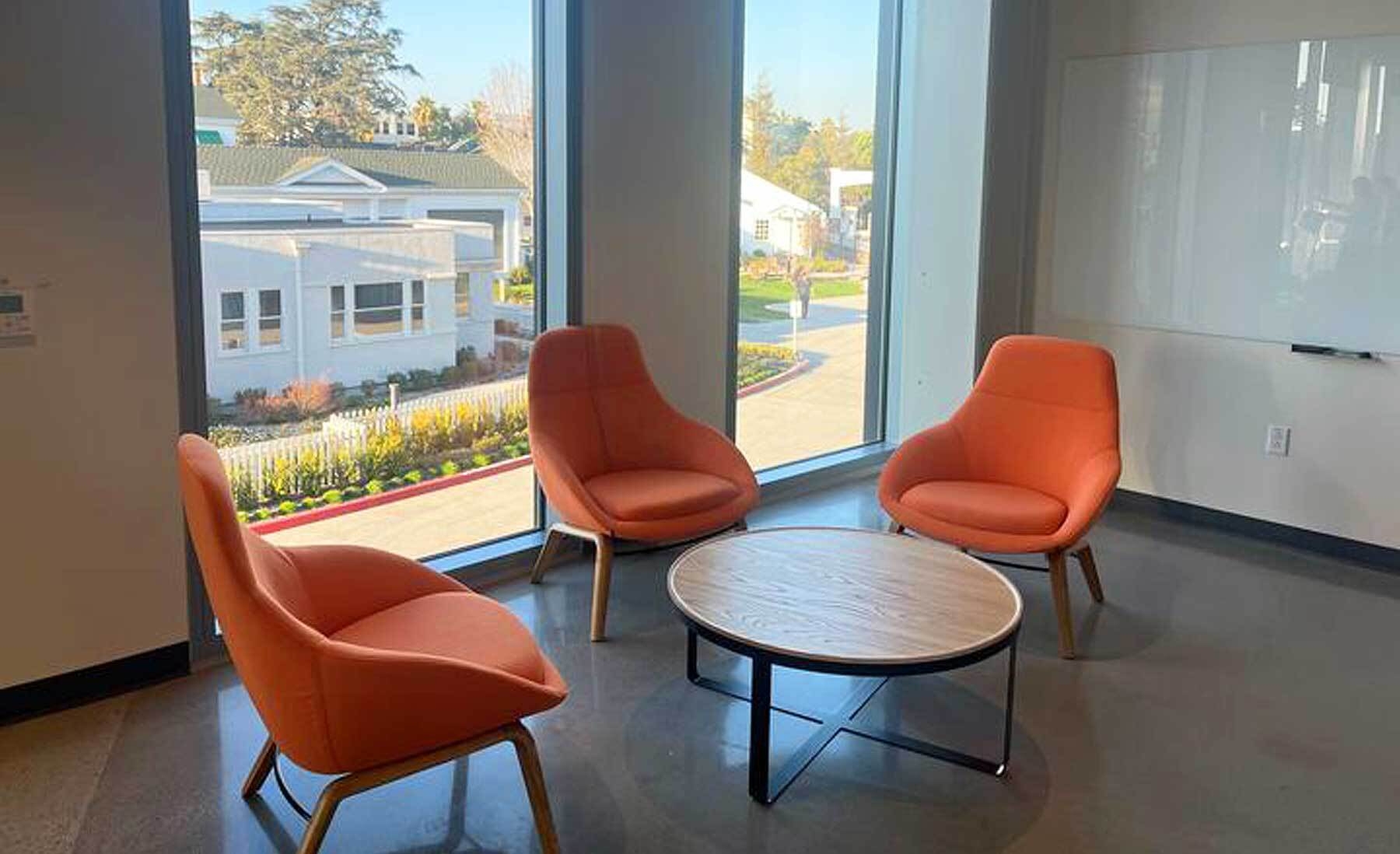 An image of a sitting area with three orange chairs and a table. You can see the Culver Studios mansion out the window. 