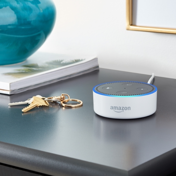 A white Amazon Echo Dot on a night stand, next to a pair of keys.