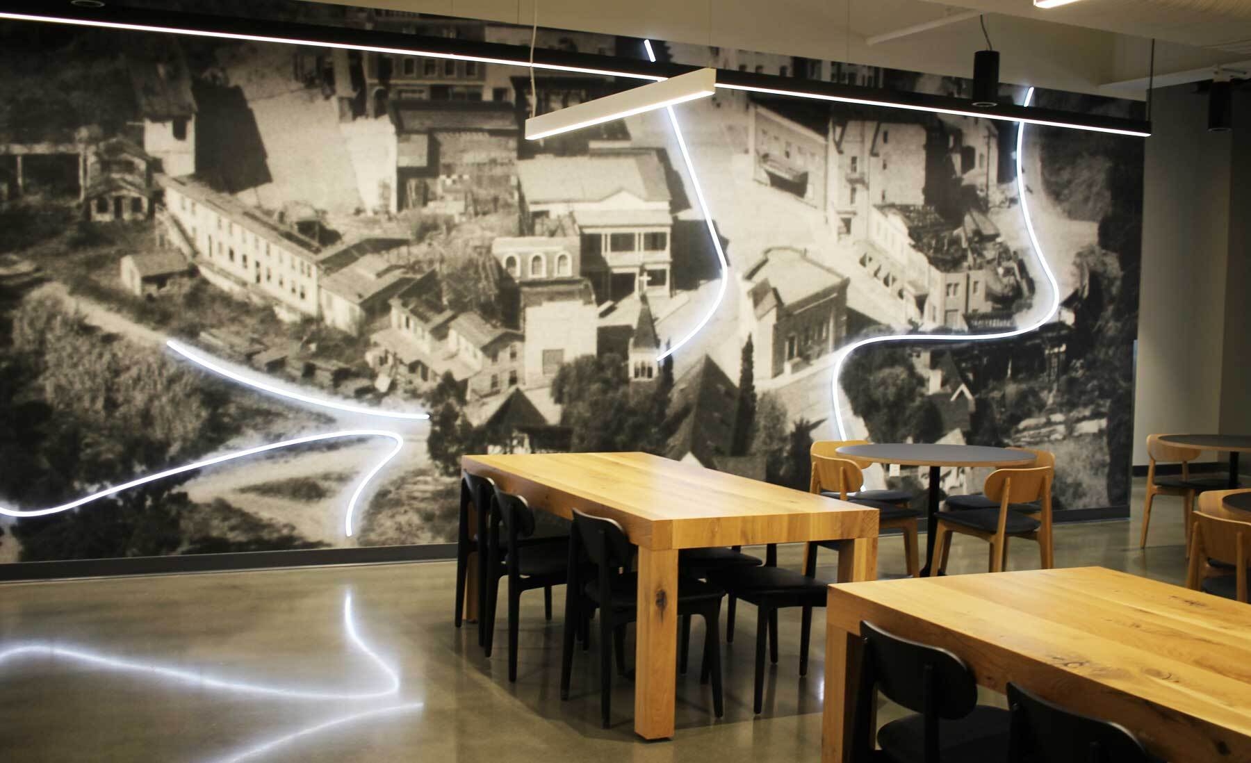 An image of a lunch room with a big mural on the wall. The mural features roads in Culver City with lights along the roads.