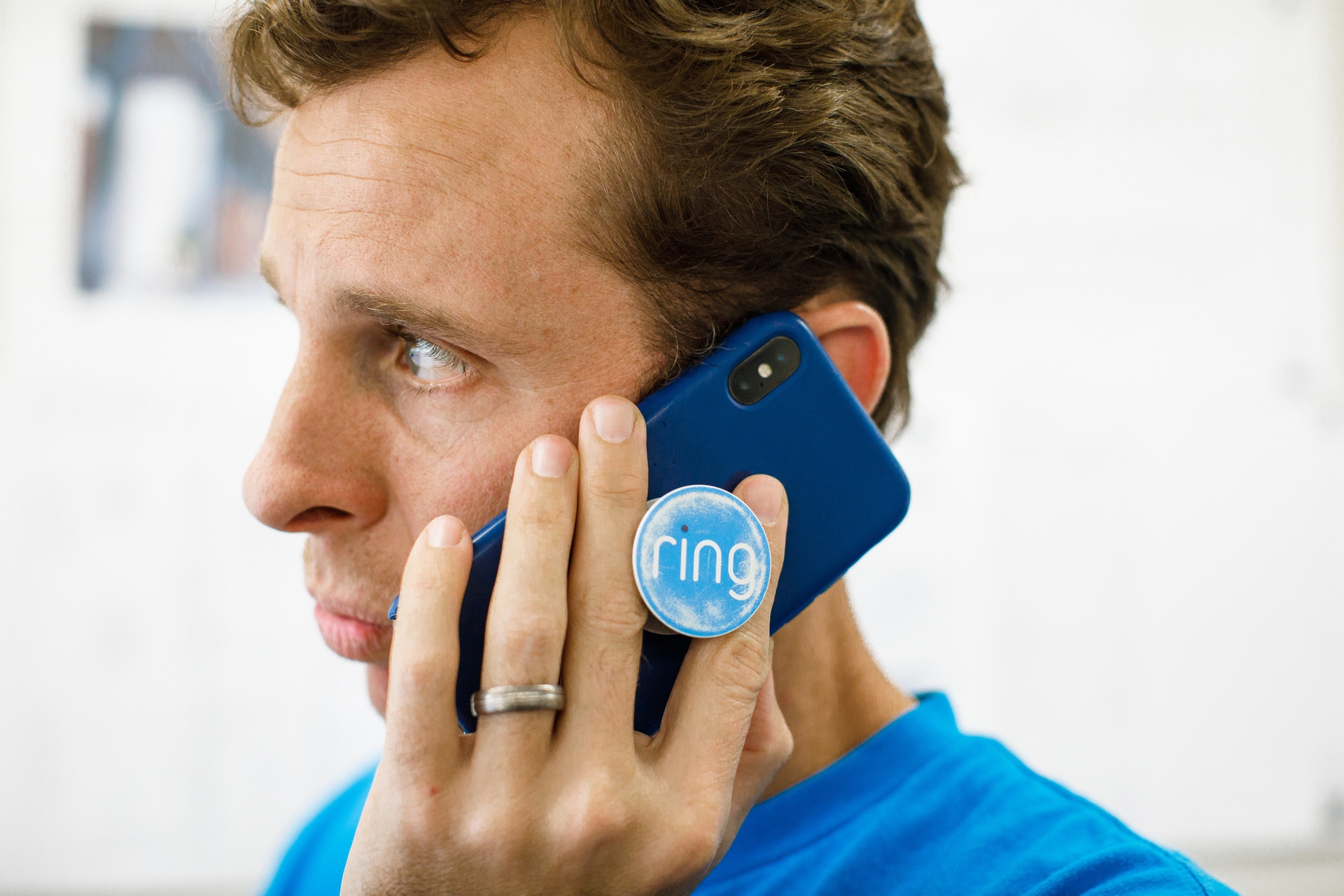 Jamie Siminoff, founder of Ring, in a blue t-shirt talks on a smartphone with a blue case. It has a Pop Socket that says Ring. 