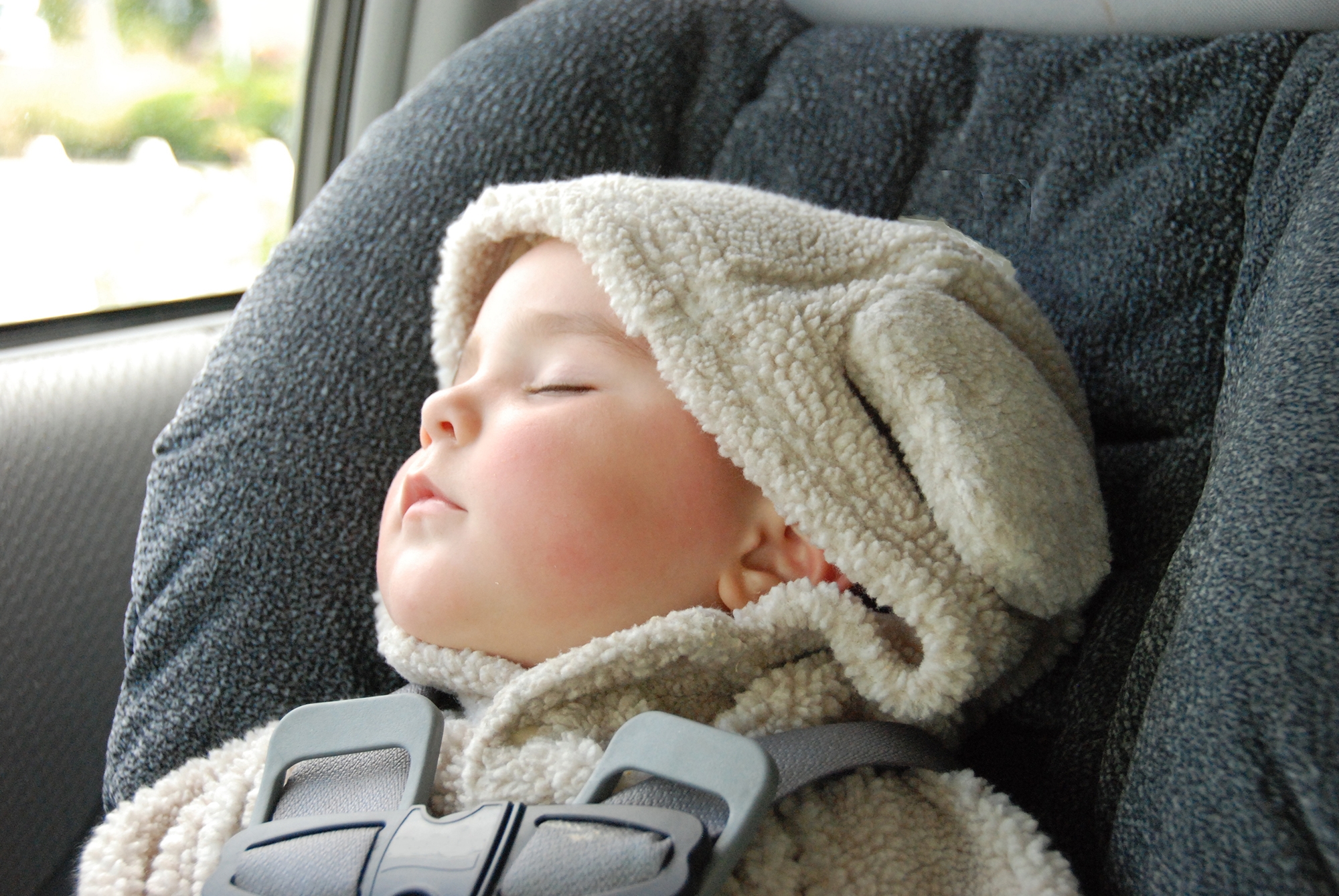 An infant wearing a hooded top with ears has fallen asleep in the carseat