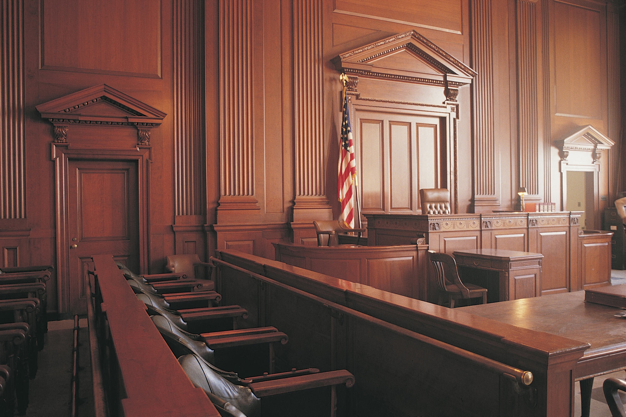 An unoccupied, architecturally striking, wood-paneled courtroom from inside the jury box, facing the Judge's bench.