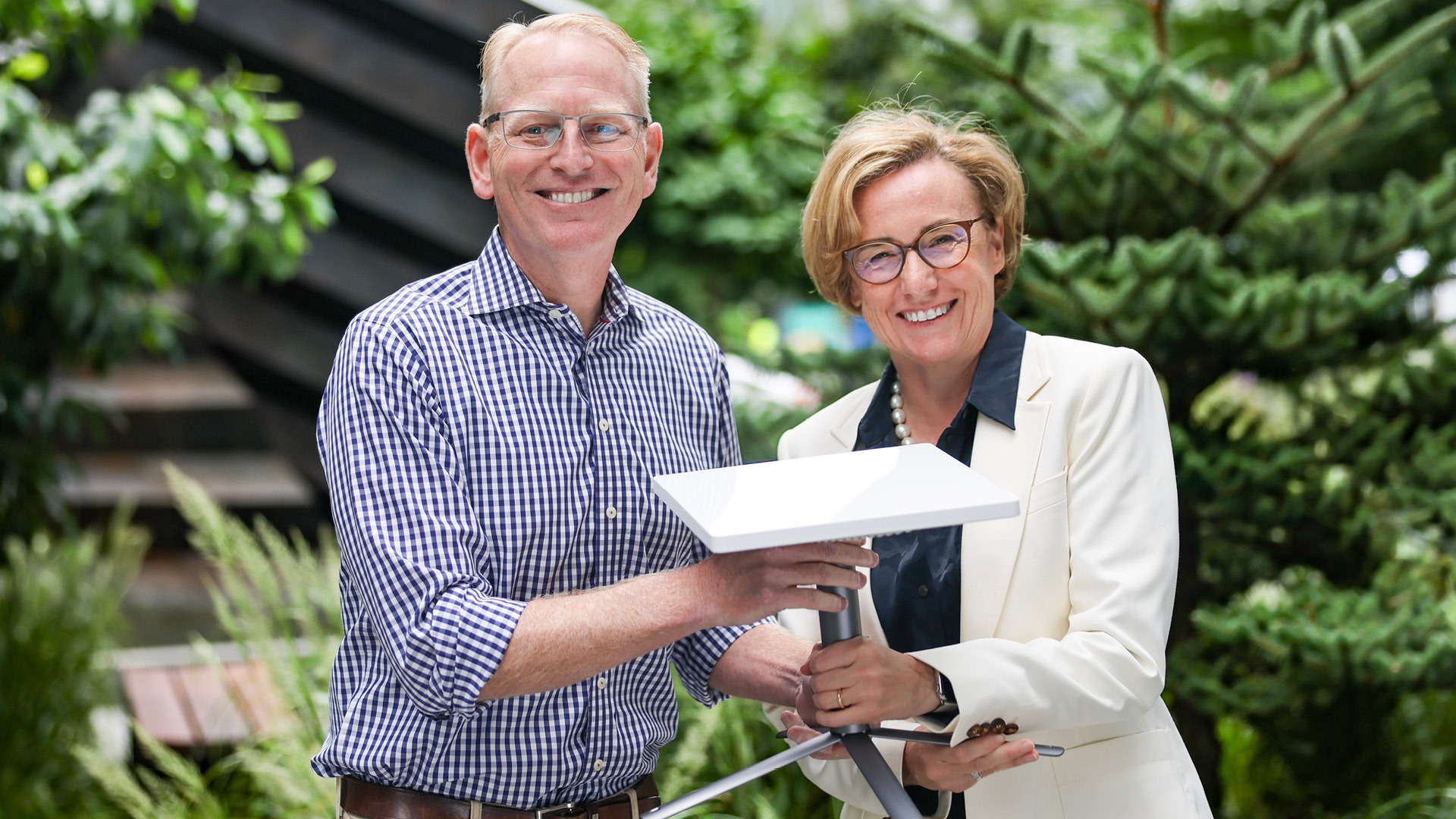 An image of Dave Limp and Margherita Della Valle holding a Project Kuiper customer terminal with plants in the background. 