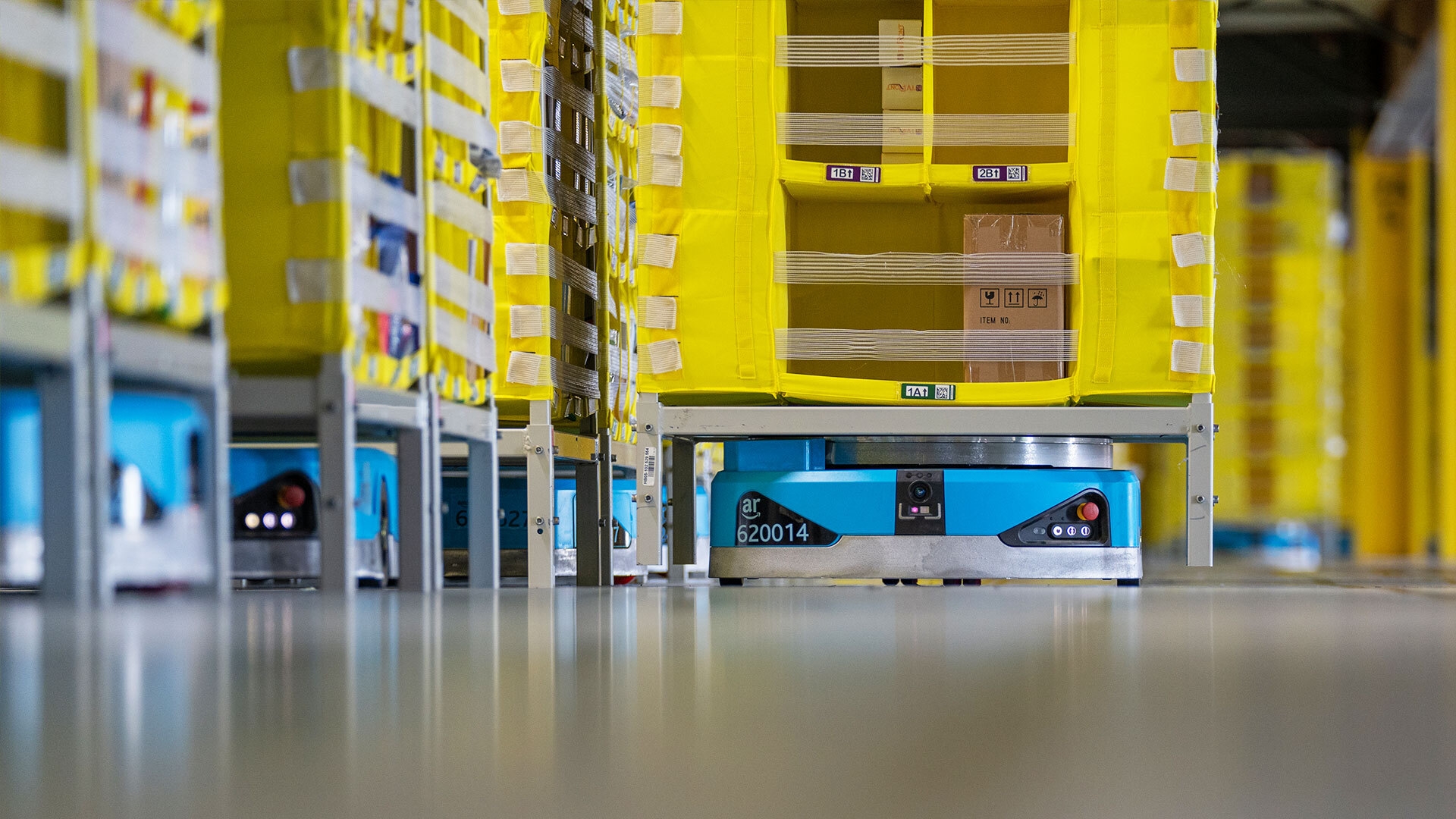 Amazon robots sit under fulfillment center racks.