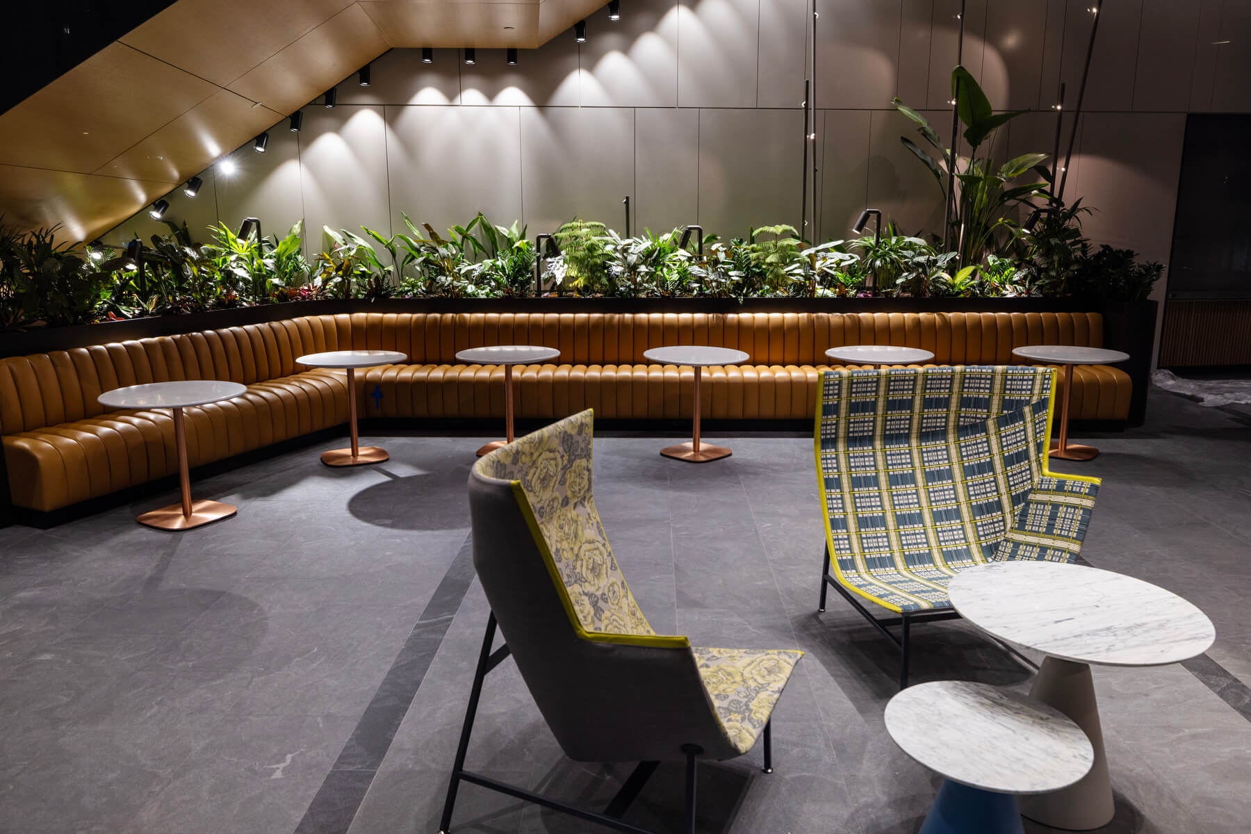 An image of a sitting area at Amazon's HQ2. There is a large booth with seating and a small table with chairs around it. There are also plants and lights in the background.