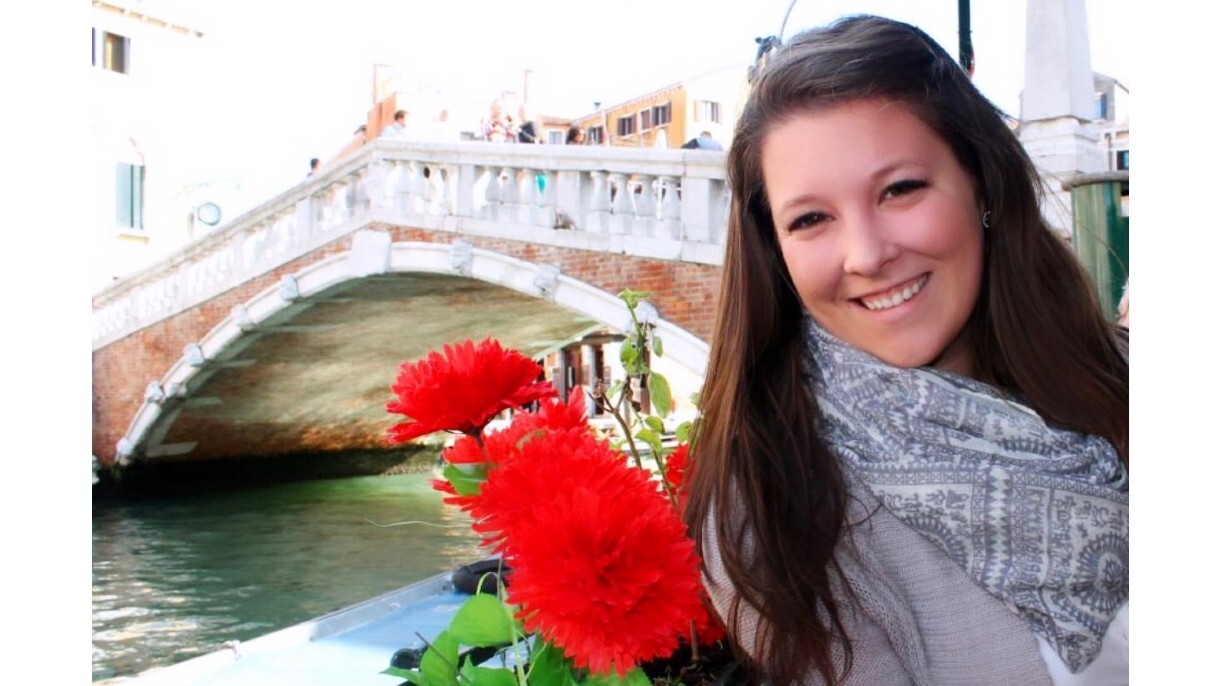 Alyssa Boggs smiles next to red flowers with a bridge and water right behind her.